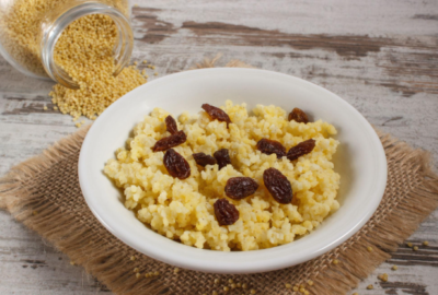Healthy millet porridge with raisins, banana slices, nuts and cinnamon for a nutritious breakfast.